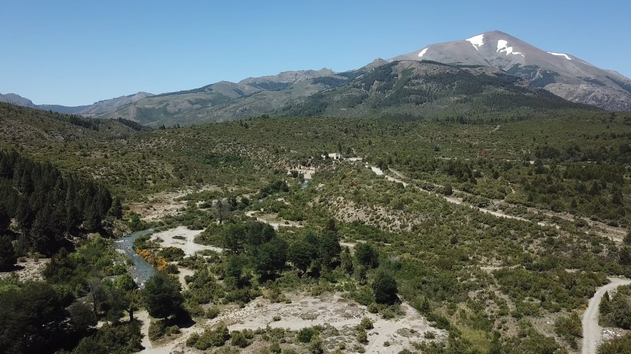 Undeveloped land with a winding creek, dirt tracks, and snow-dusted mountains.