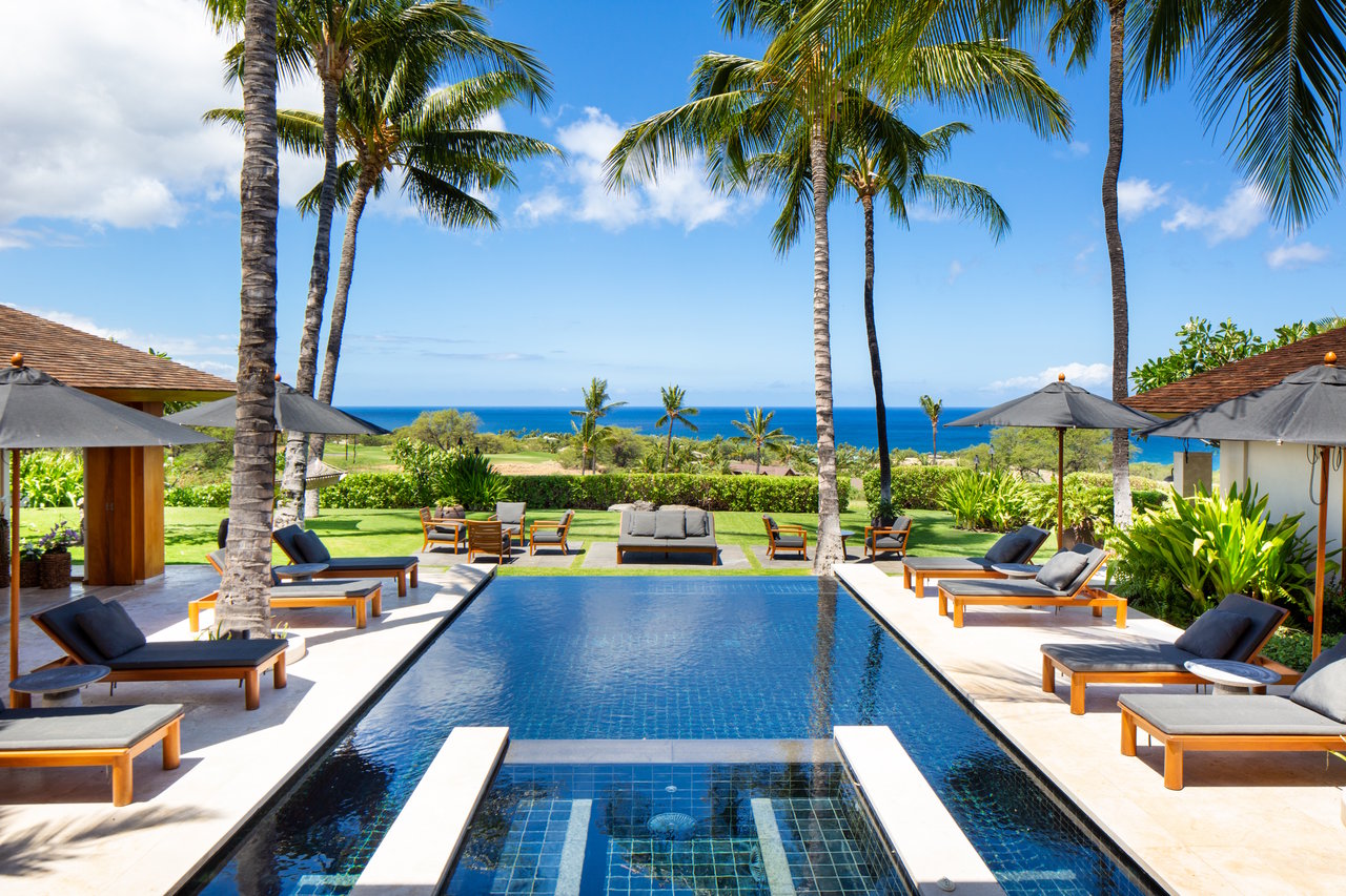 Outdoor pool framed by palm trees and lounge chairs, with ocean views beyond.