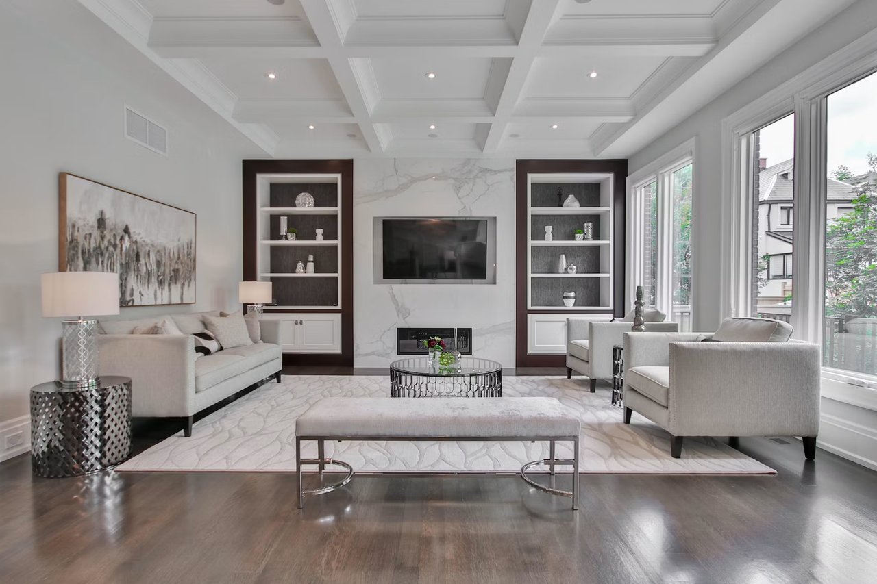 Living room with a coffered ceiling, marble fireplace wall, built-in shelves, and large windows.