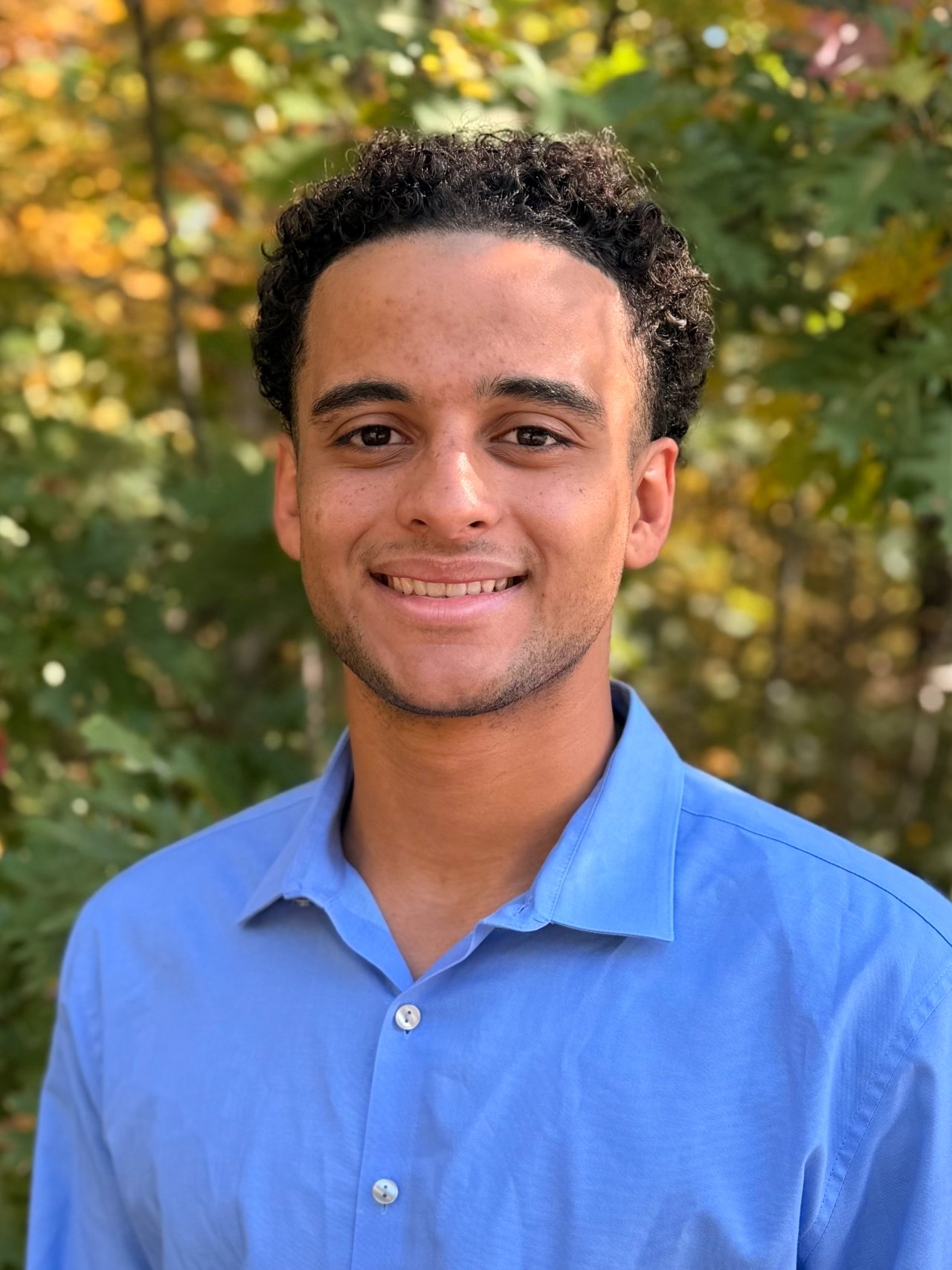 Evans Sterling smiling in a blue shirt against autumn foliage.