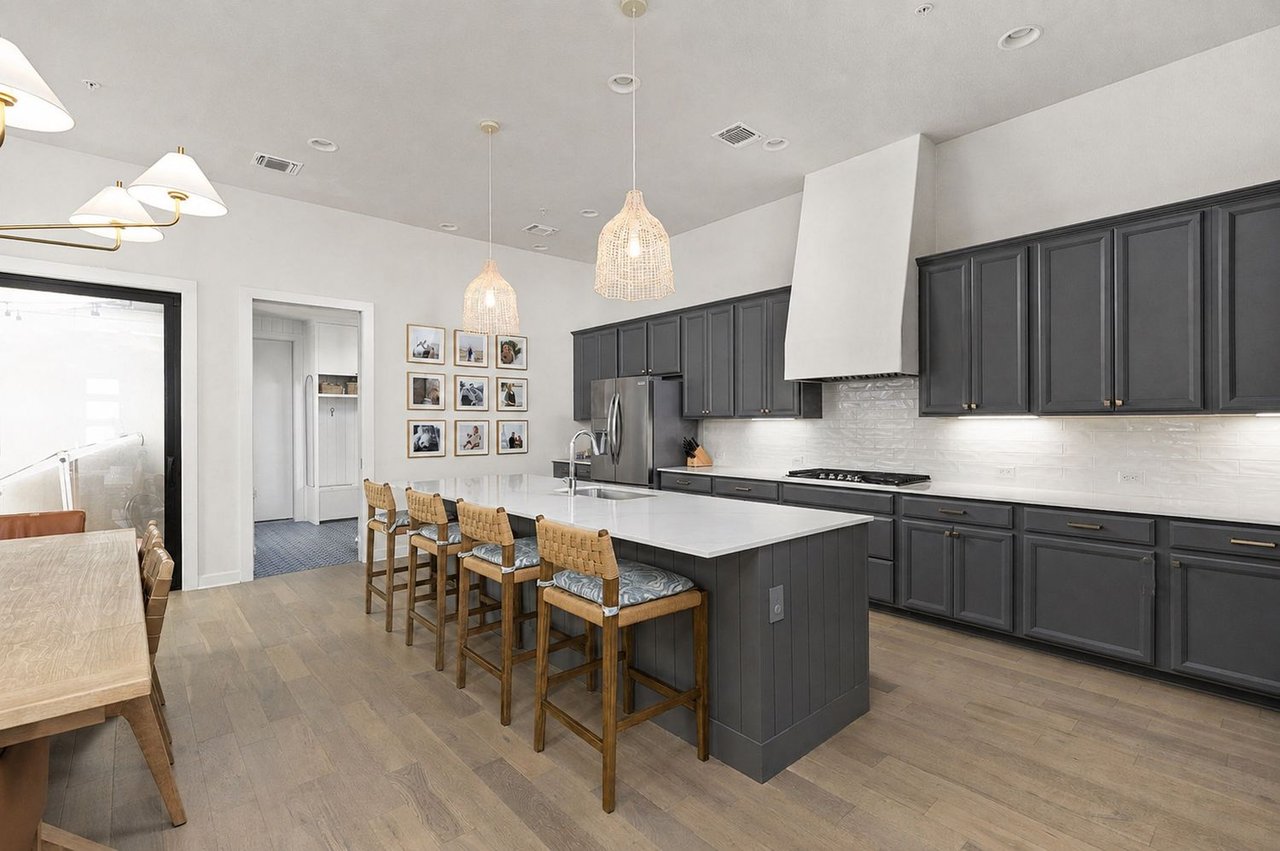 Kitchen with charcoal cabinets, a large white island, woven-seat stools, and a dining table by a glass door.