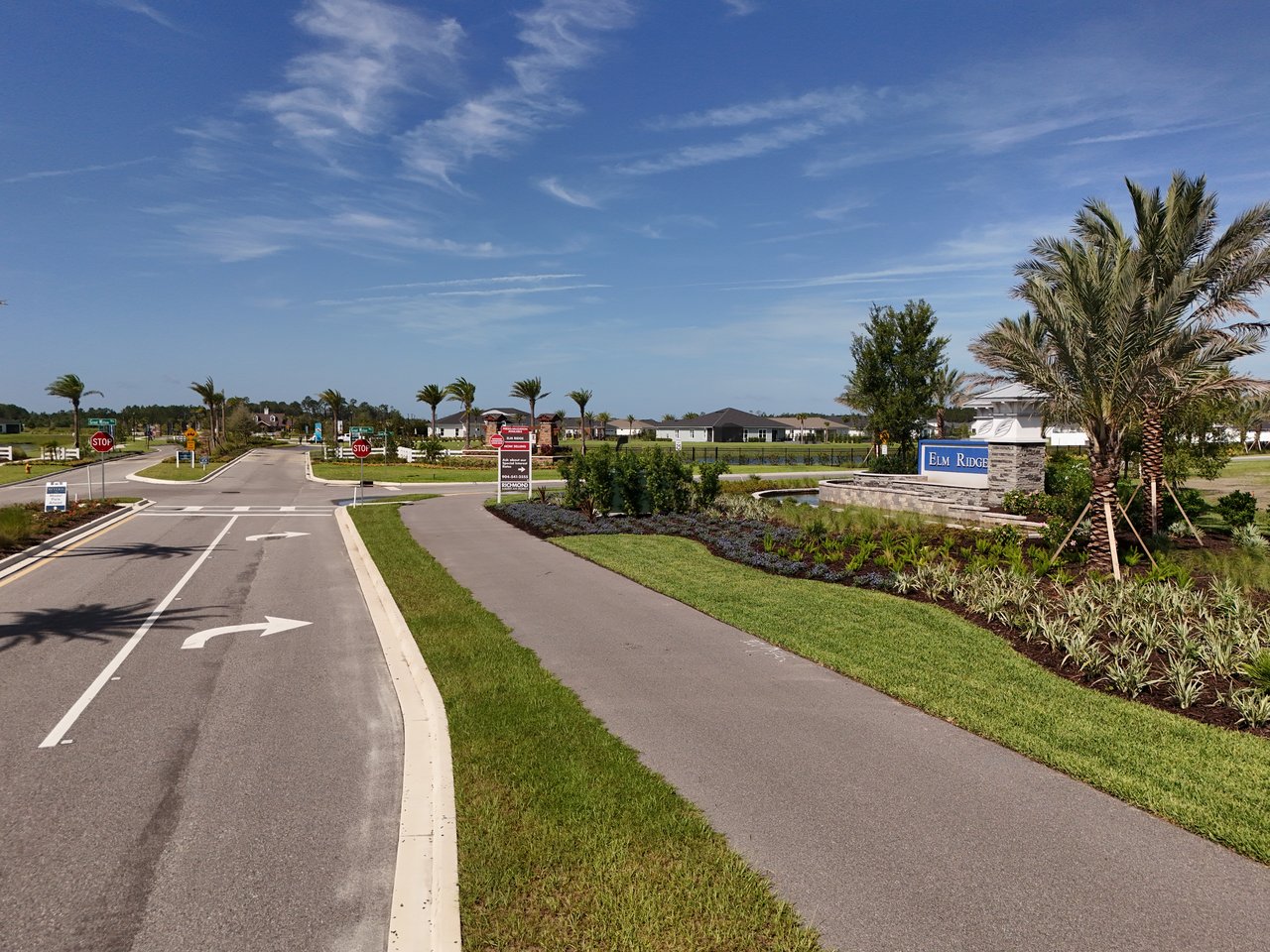 Elm Ridge community entrance with a stone monument sign, palm trees, and homes beyond.