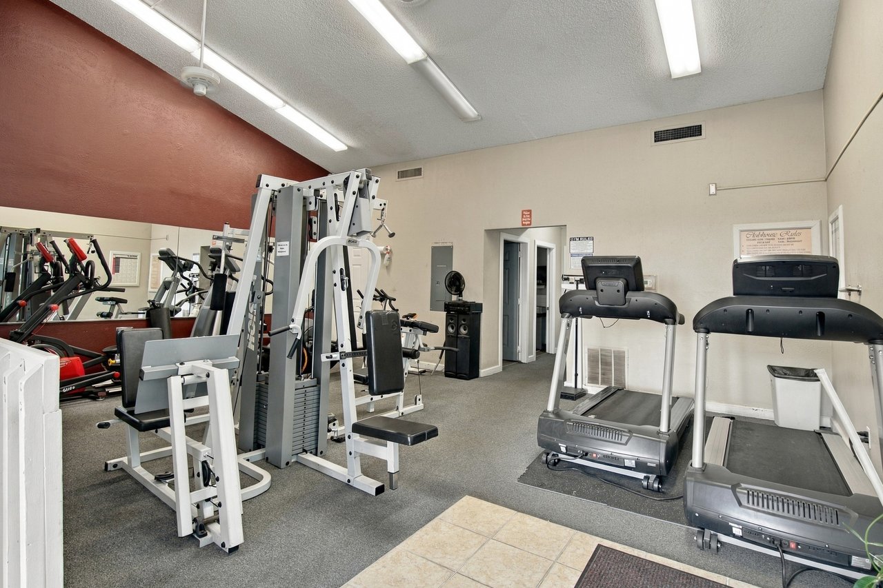 Fitness room with weight machines, exercise bikes, two treadmills, and a mirrored wall.