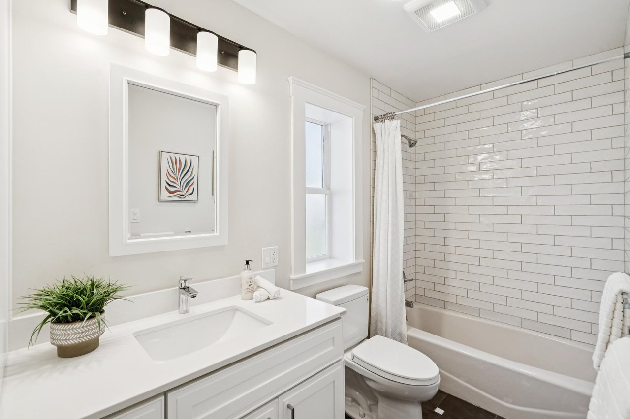 Bright bathroom with a white vanity, framed mirror, and subway-tiled tub and shower.