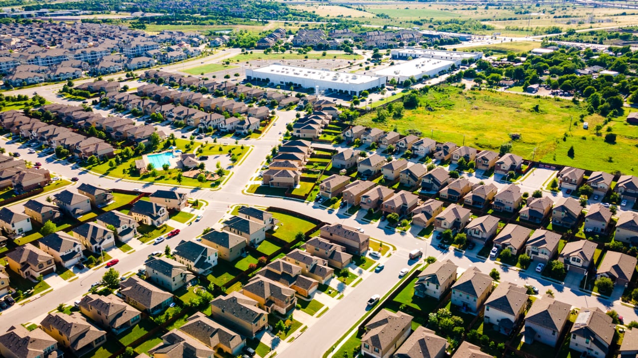 Aerial view of a suburban neighborhood with homes, streets, and open green space at sunset.