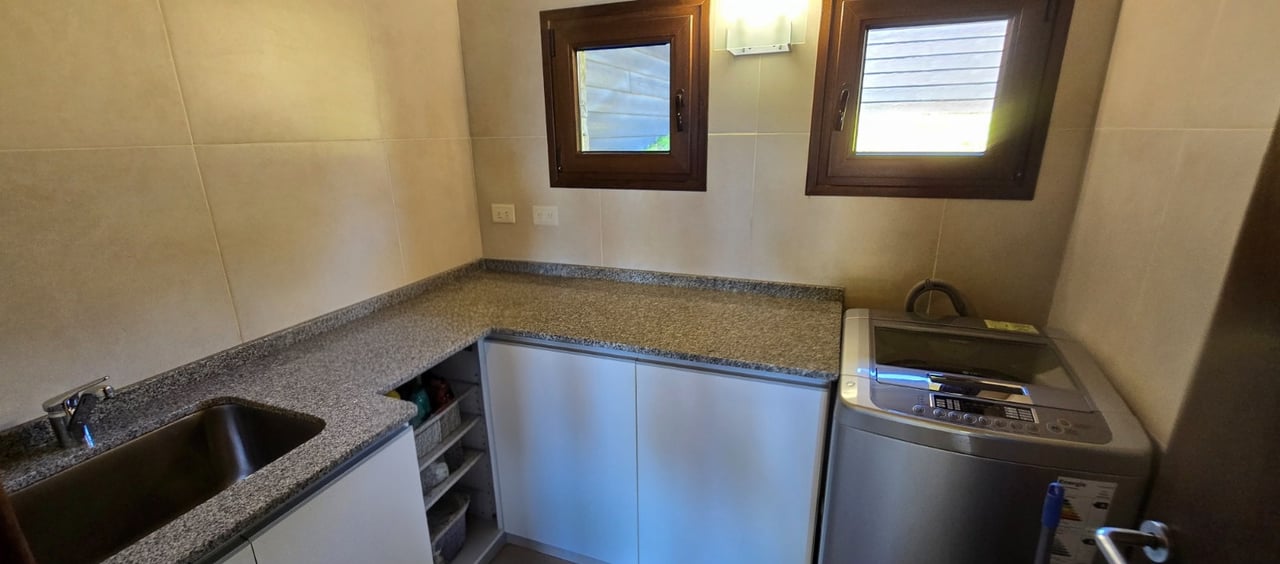 Laundry room with a top-loading washer, stainless-steel sink, granite counters, and two windows.