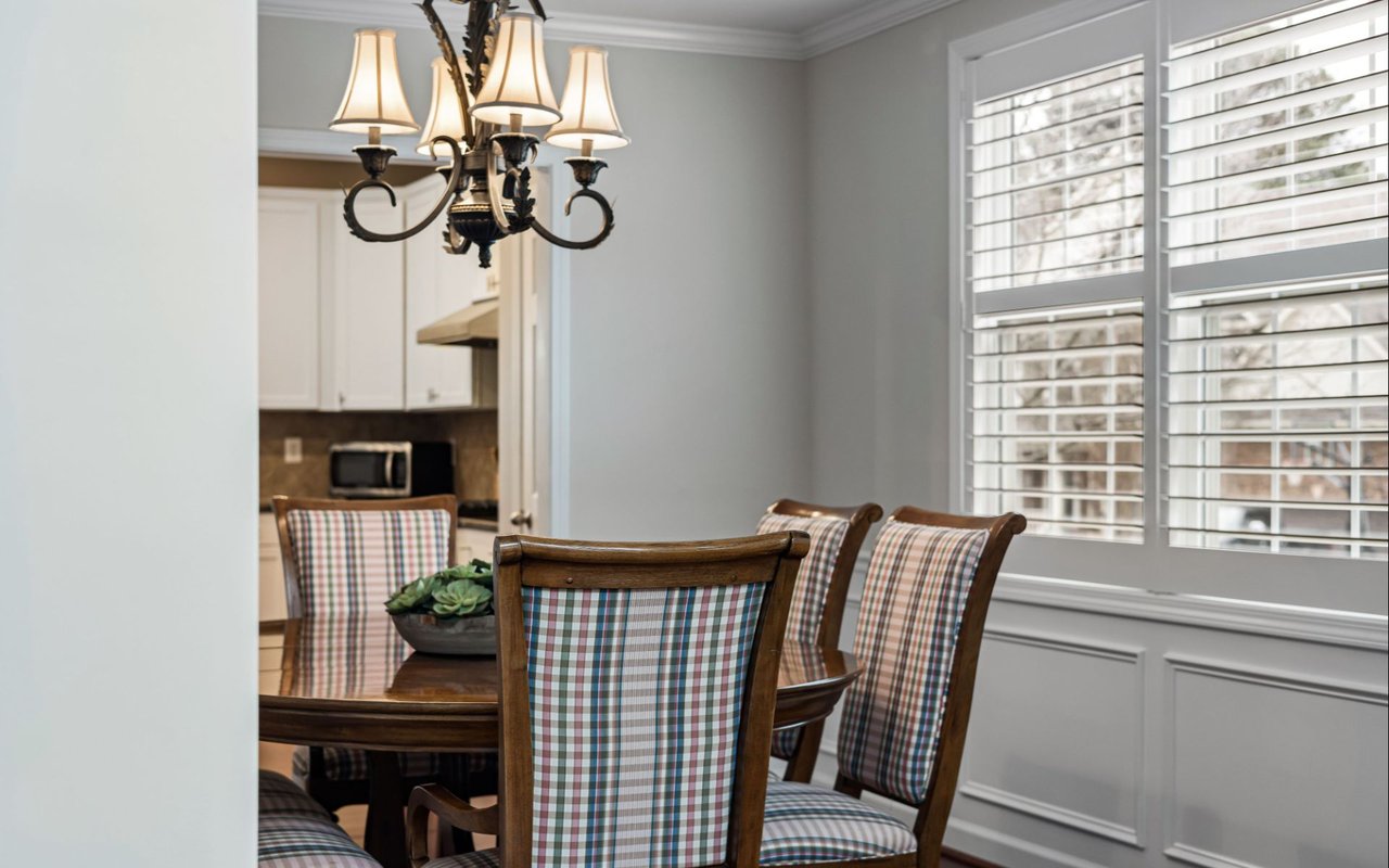 Dining room with plaid chairs, a dark wood table, and windows with plantation shutters.