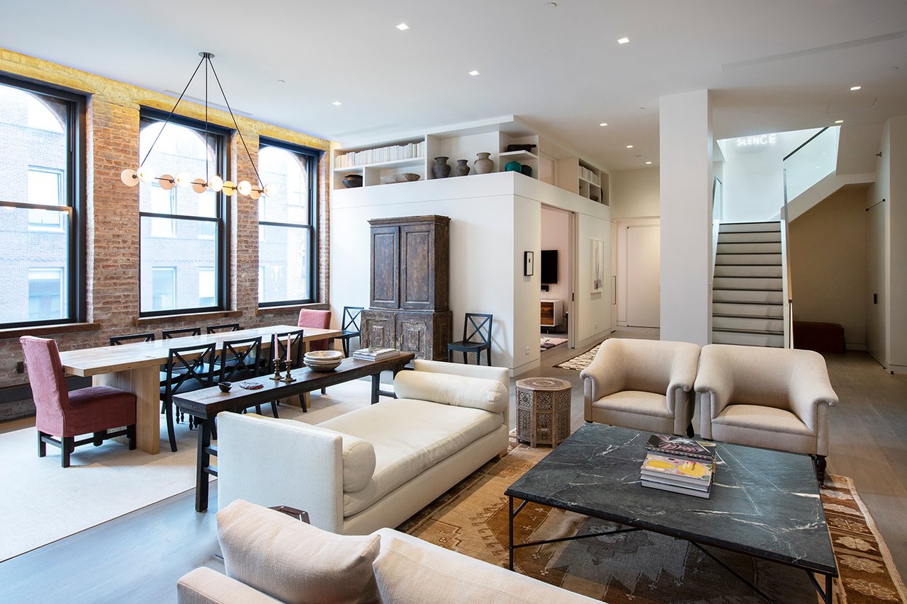 Spacious living area with a white sofa and marble coffee table, adjacent to a long wooden dining table illuminated by a modern globe chandelier.
