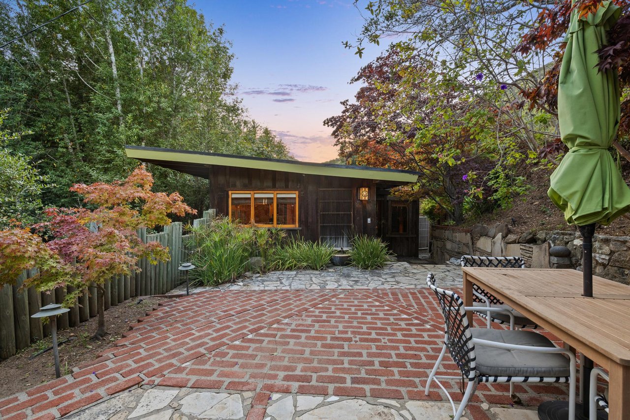 Mid-century modern home with green roofline and brick patio surrounded by fall foliage and outdoor dining area at dusk, Big Sur.