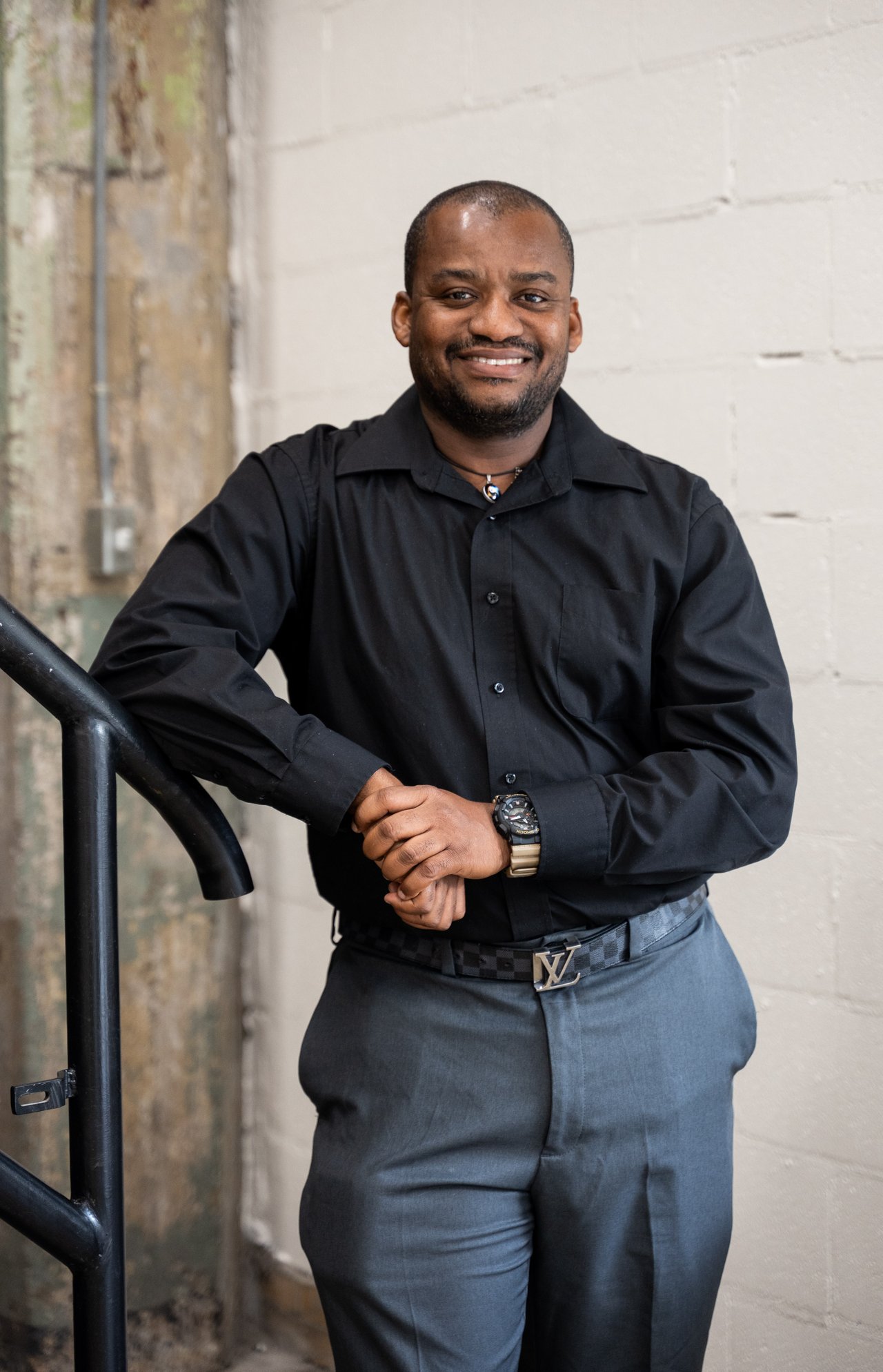 Gerson Sixieme standing by a railing in a black shirt and gray trousers.