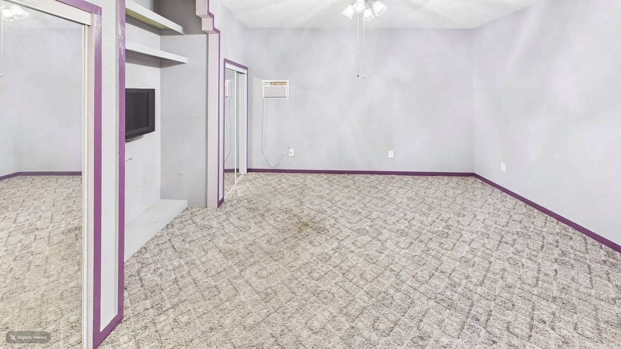Empty bedroom with patterned carpet, purple-trimmed mirrored closet doors, and a wall-mounted television.