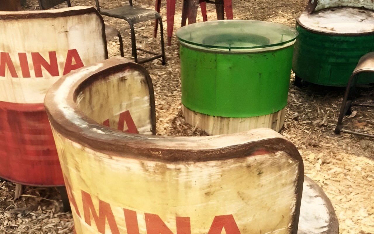 Weathered barrel chairs and green glass-topped barrel table on wood chips.