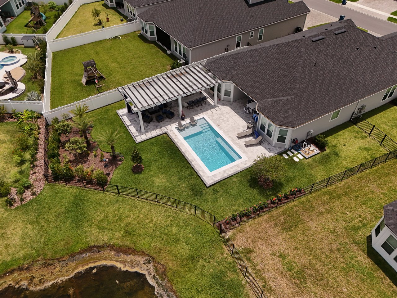 Aerial view of a home with a fenced backyard, swimming pool, and covered patio beside a waterway.