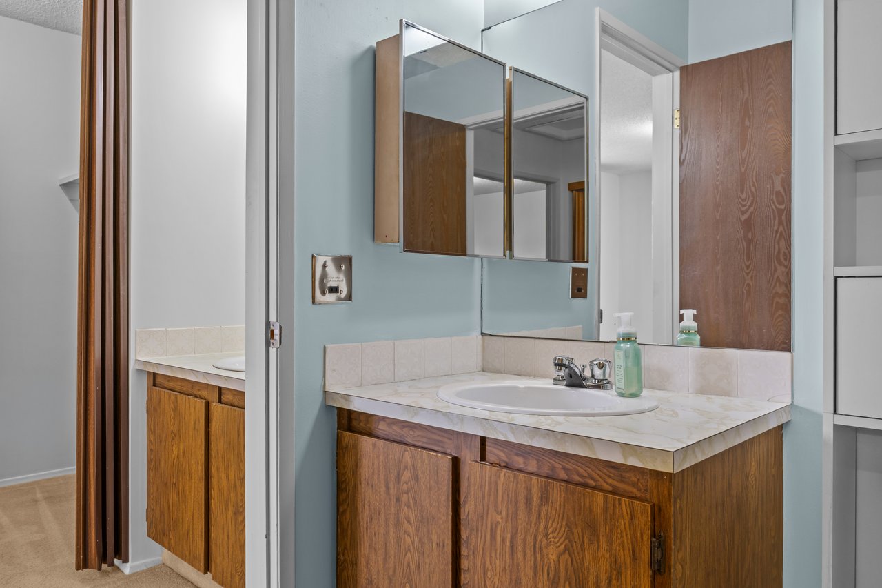 Bathroom vanity with wood cabinets, an oval sink and mirrored medicine cabinets.
