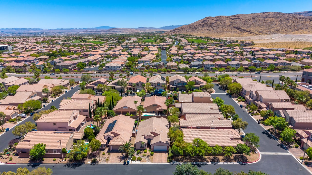 Aerial view of tiled-roof homes and residential streets with desert mountains beyond.