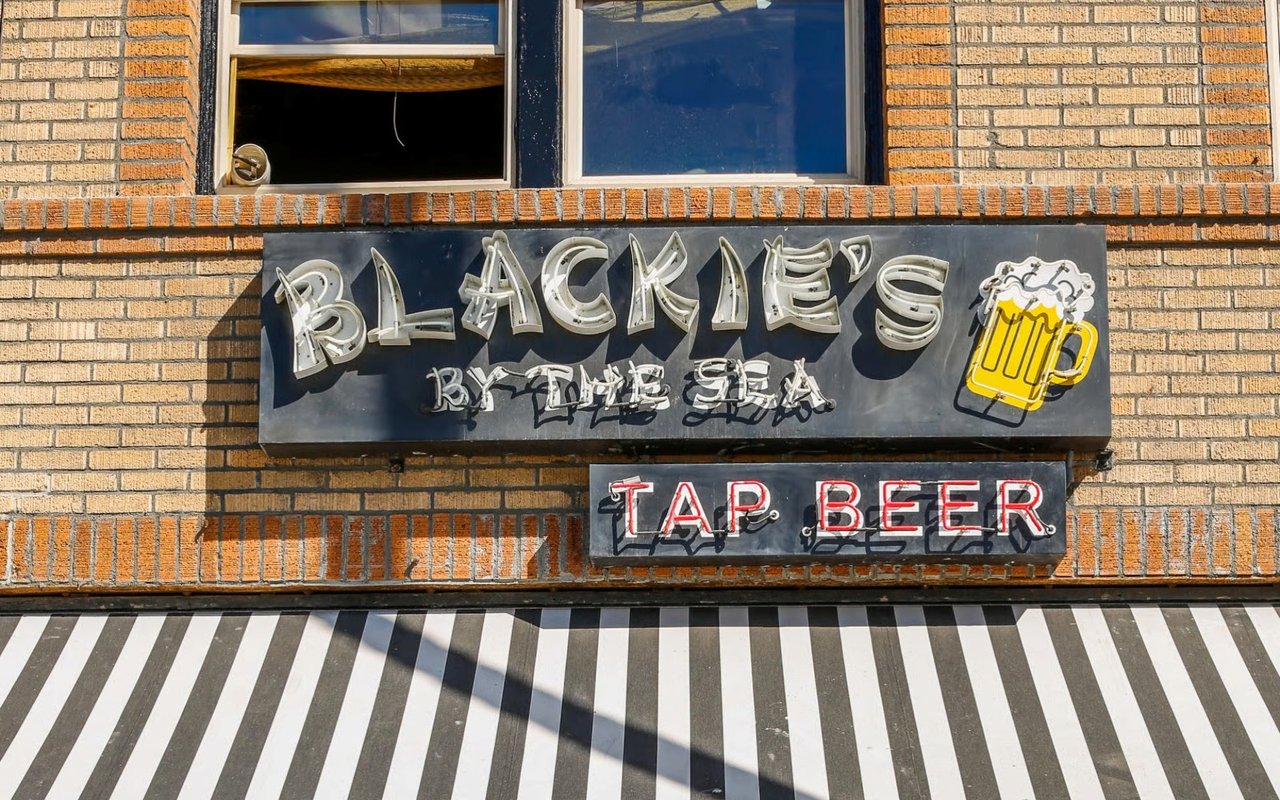 A nostalgic sign for a "tap beer" bar on a brick building features a bright yellow beer mug, conveying a welcoming mood.
