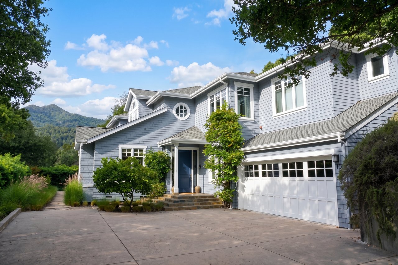 Gray two-story house with a white garage, landscaped driveway, and wooded mountain backdrop.