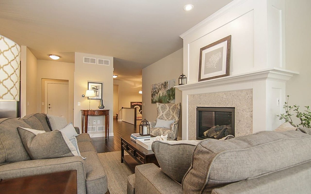 Furnished living room with gray sofas, a large white fireplace, and a patterned armchair.