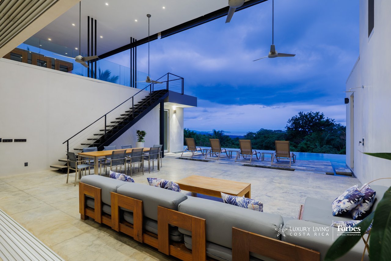 Open-air terrace with lounge seating, an infinity pool, and distant ocean views at dusk.