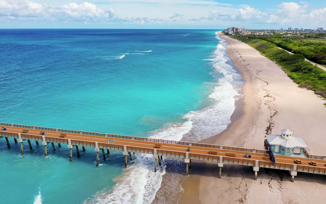 Aerial view of Juno Beach with turquoise water, sandy shoreline, and a fishing pier.