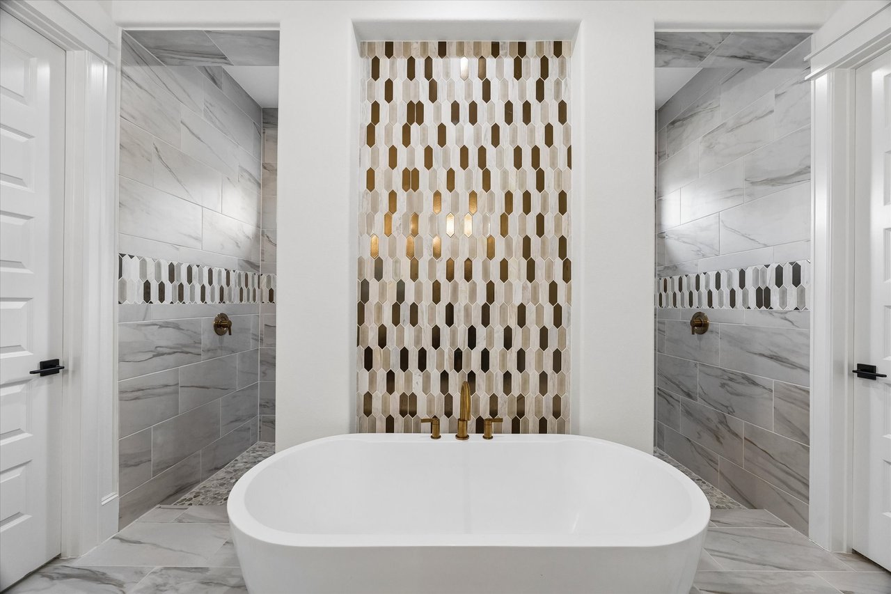 Freestanding tub between two marble-look showers, with a gold-and-white geometric tile feature wall.