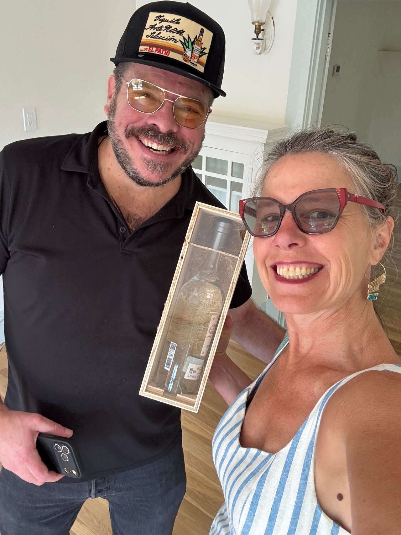 Smiling man and woman pose together while holding a boxed bottle.