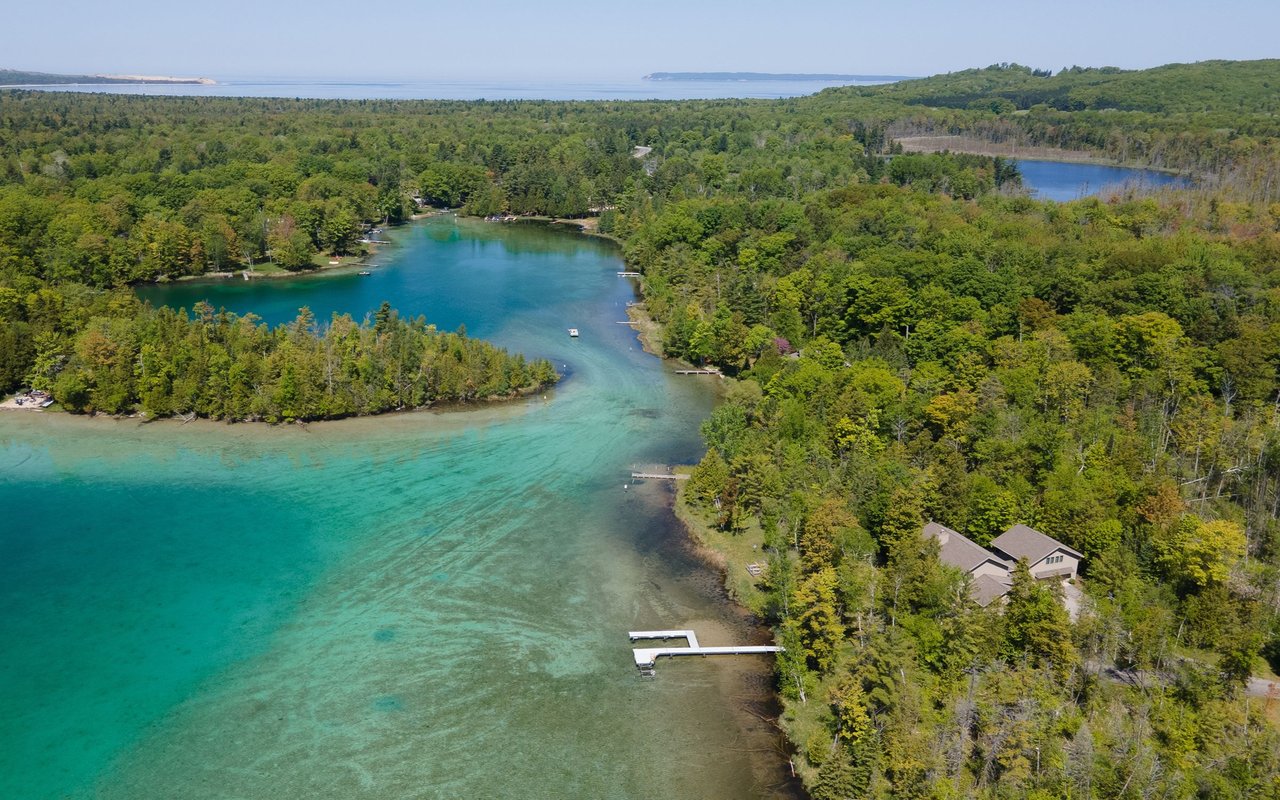 Aerial view of a turquoise waterway winding through forest, with docks and a lakeside home.