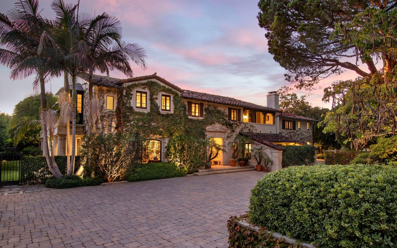  A magnificent, multi-story Mediterranean-style mansion with a red-tiled roof and stone facade, partially covered in vibrant green ivy.