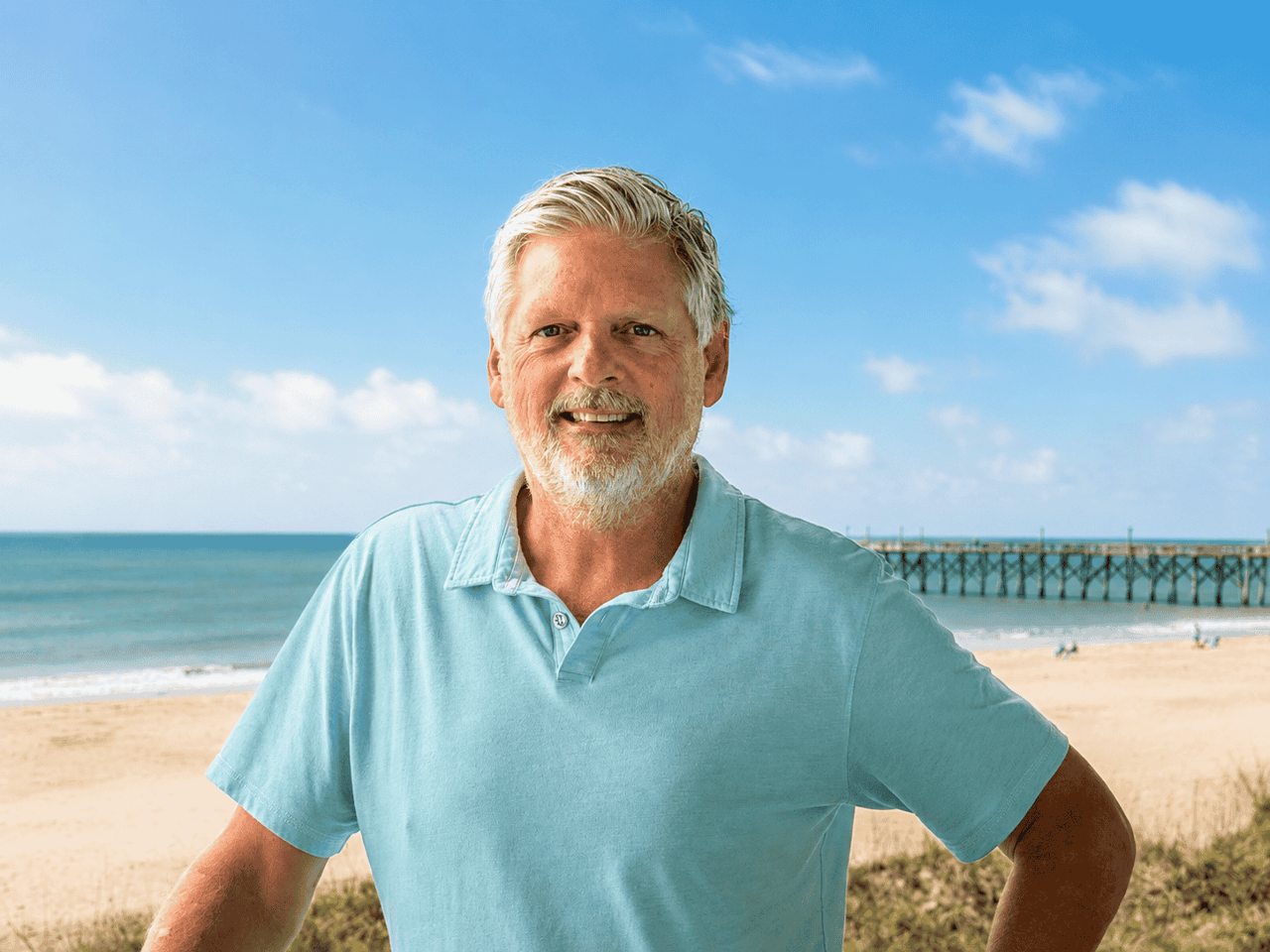 John Arnett standing on a beach in a light blue polo shirt.