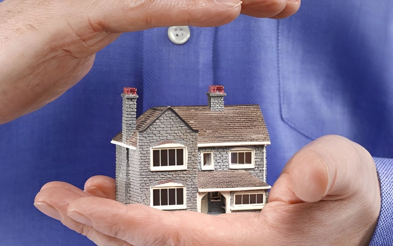 Hands sheltering a miniature stone house, illustrating protection for a home.