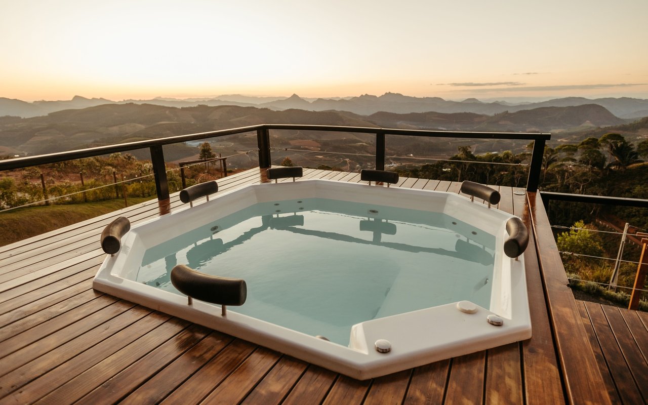 Outdoor hot tub on a wooden deck overlooking layered mountain ridges at sunset.
