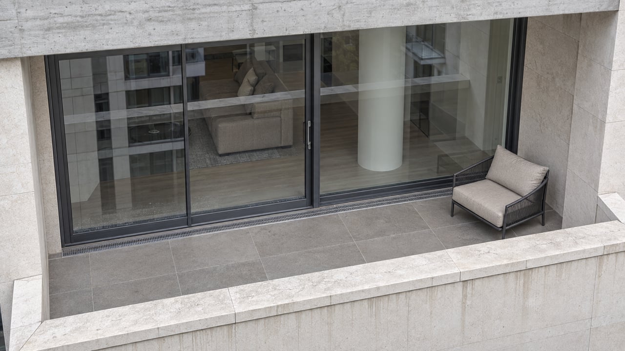 Elevated view of a contemporary condominium balcony with a pale stone parapet, closed glass doors and one cushioned lounge chair.