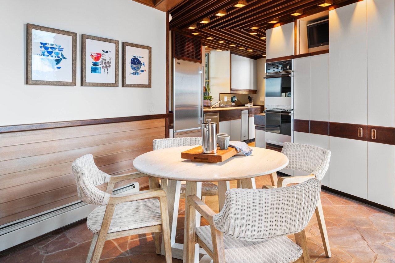 Kitchen and dining area with a round table, woven chairs, stainless steel appliances, and a wood-beamed ceiling.
