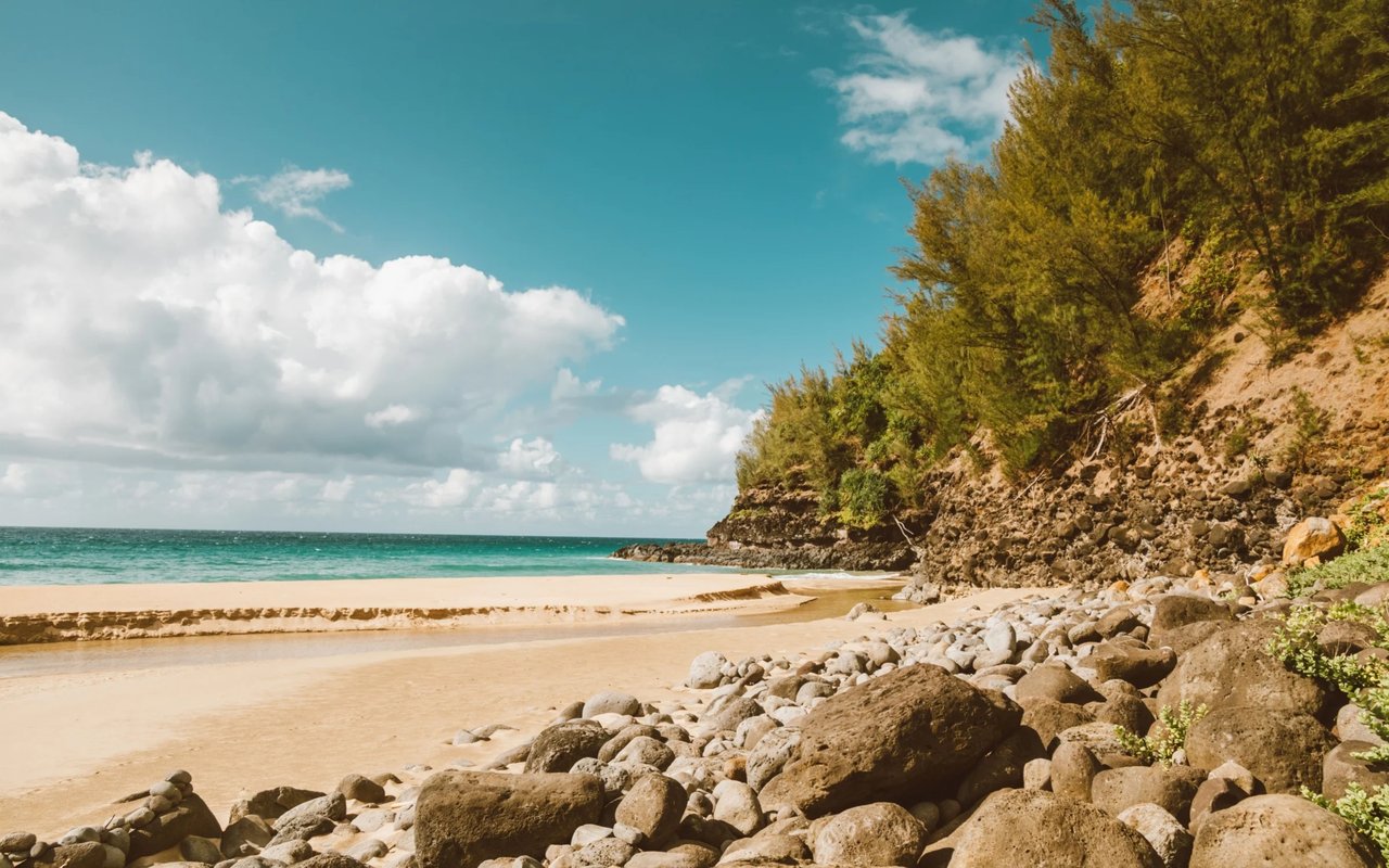 Wailupe Beach with turquoise water, a sandy shore, and a rocky, tree-lined bluff.