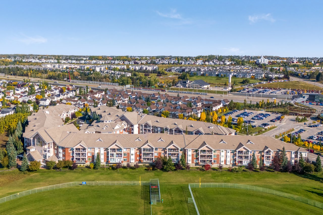Aerial view of a multi-building apartment complex beside a sports field and parking lots.