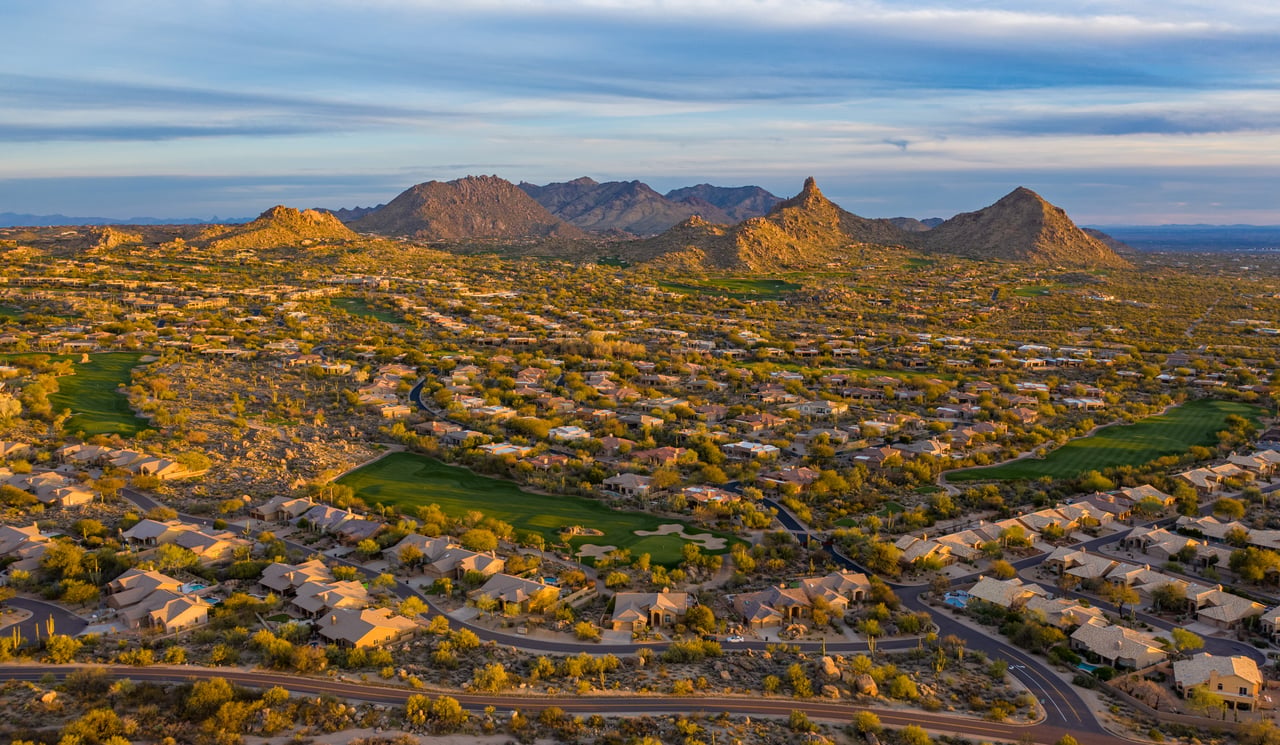 Arcadia homes and golf courses spread beneath rugged desert mountains at golden hour.