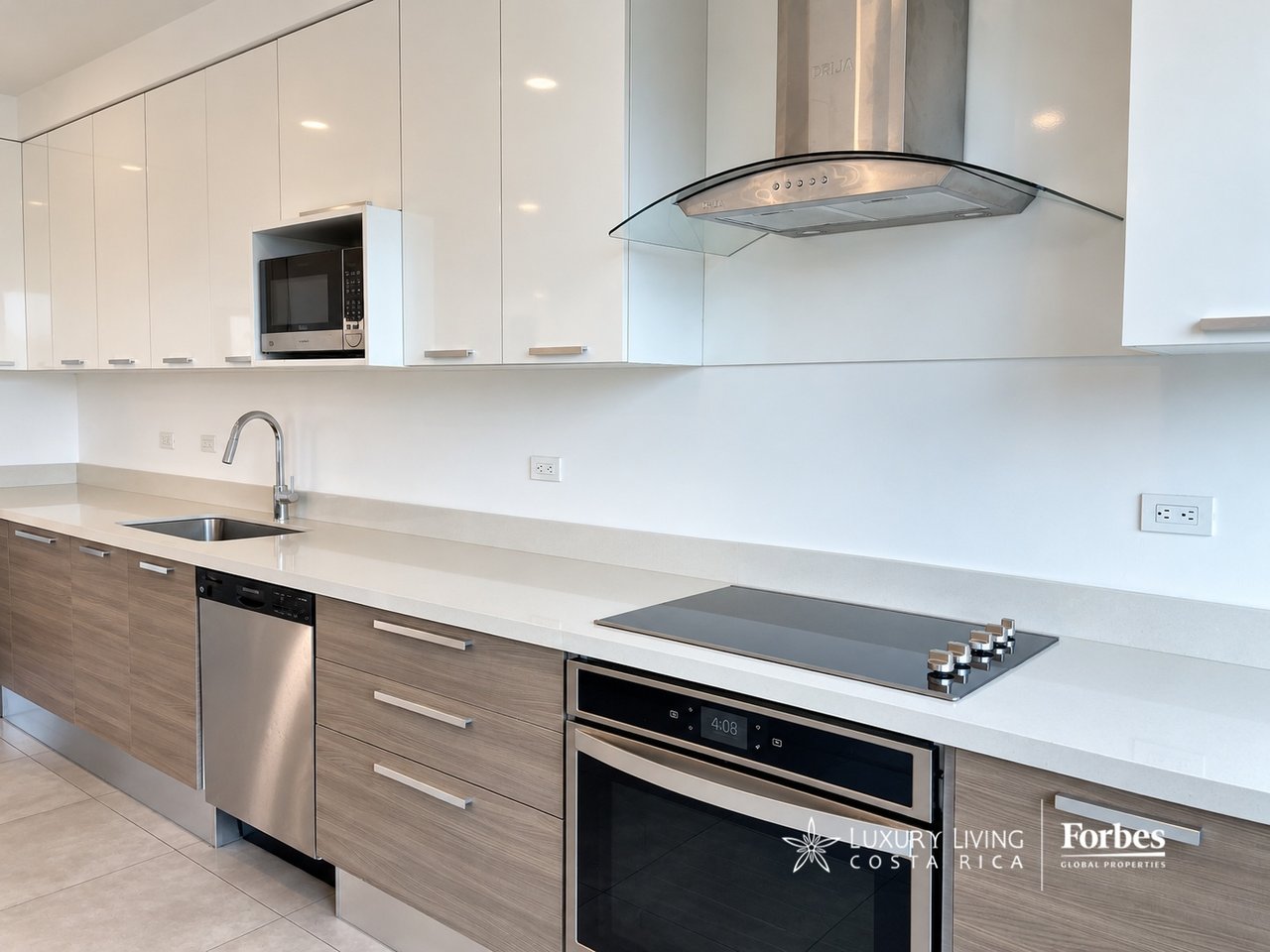Modern kitchen with white cabinets, wood-tone drawers, stainless steel appliances, and a glass-canopy range hood.