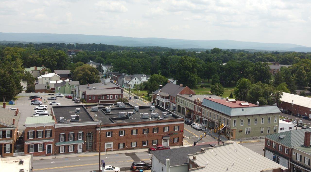 An elevated aerial drone shot looking down at the historic brick buildings, tree-lined streets, and surrounding countryside of downtown Berryville, VA in Clarke County, captured by local real estate expert Diane Geremia.