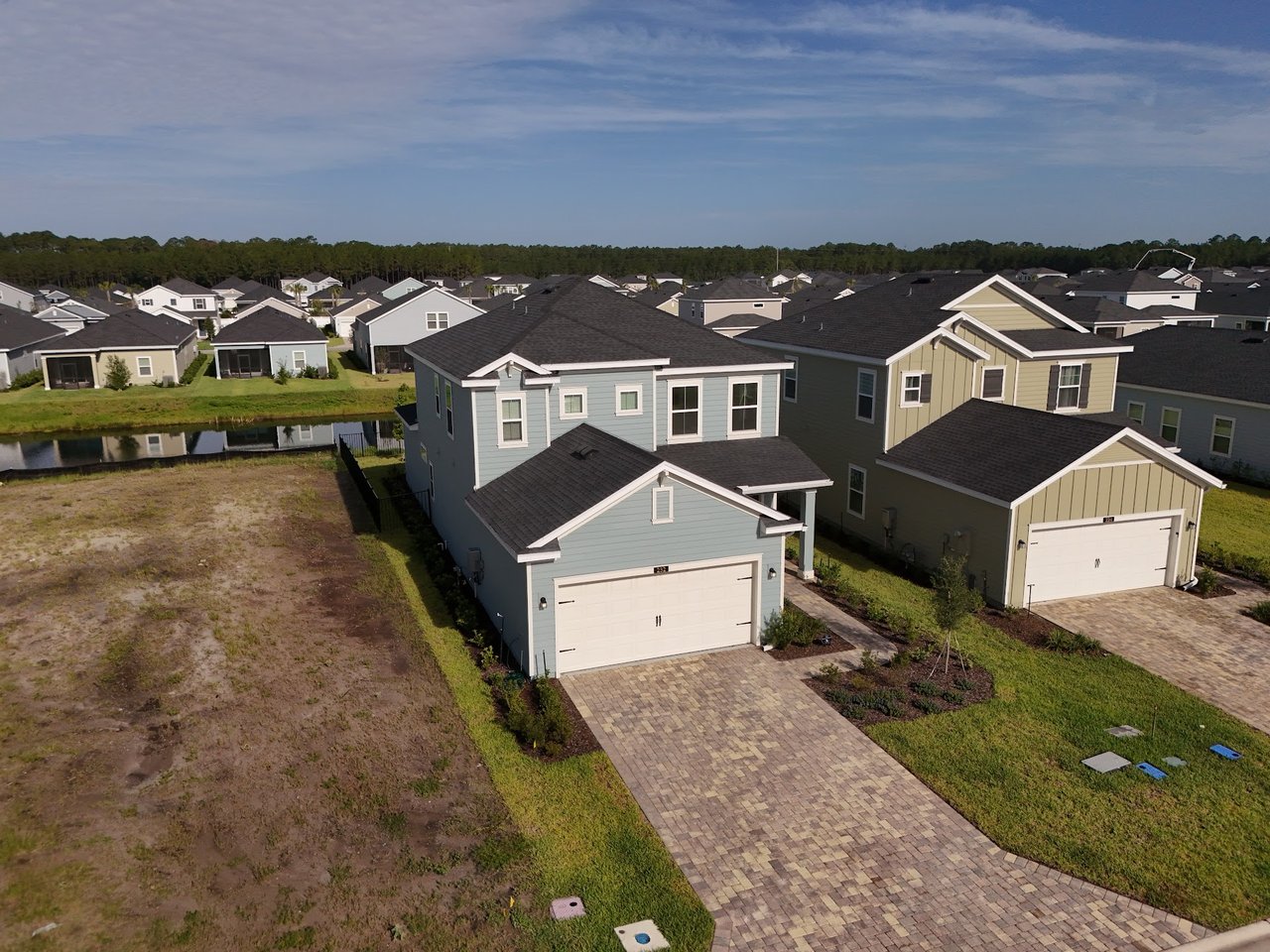 Aerial view of two-story homes beside a pond and undeveloped lot.