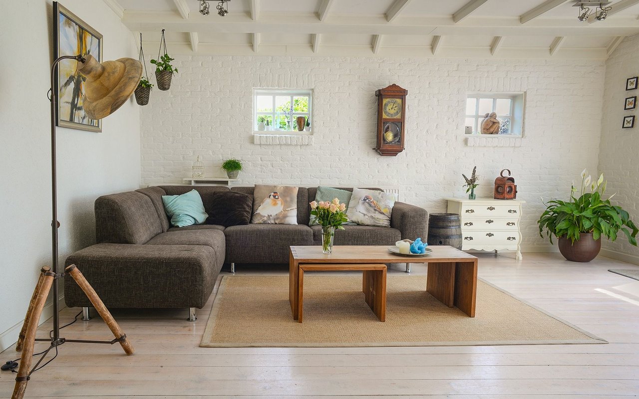 Living room with a gray sectional, white brick walls, exposed beams, and a wooden coffee table.