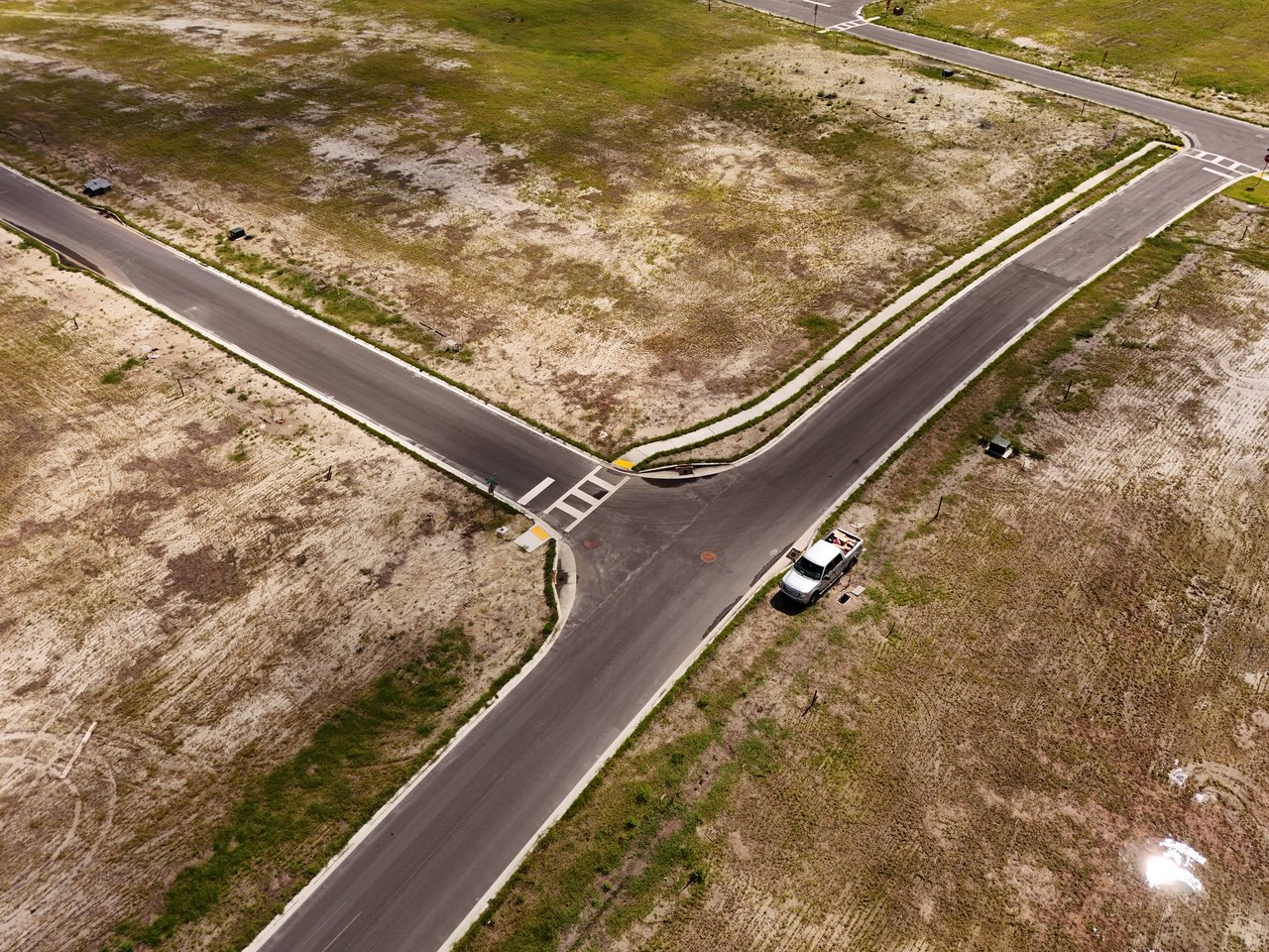 Aerial view of vacant sandy lots and a newly paved road intersection.