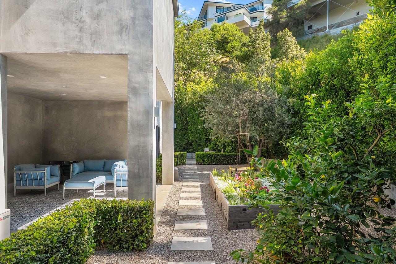 Covered patio with blue seating beside a gravel path and raised flower bed.