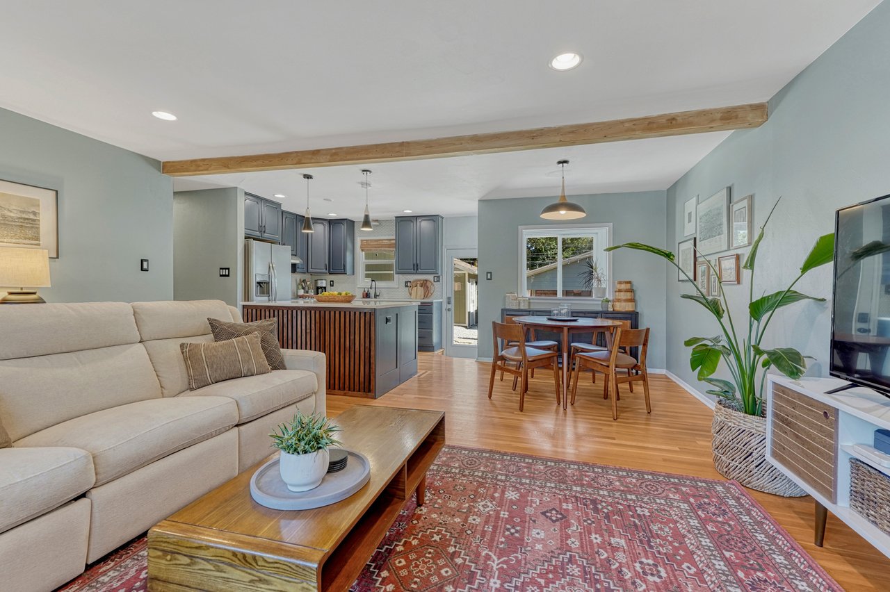 Living room open to the dining area and kitchen, with an exposed wood ceiling beam