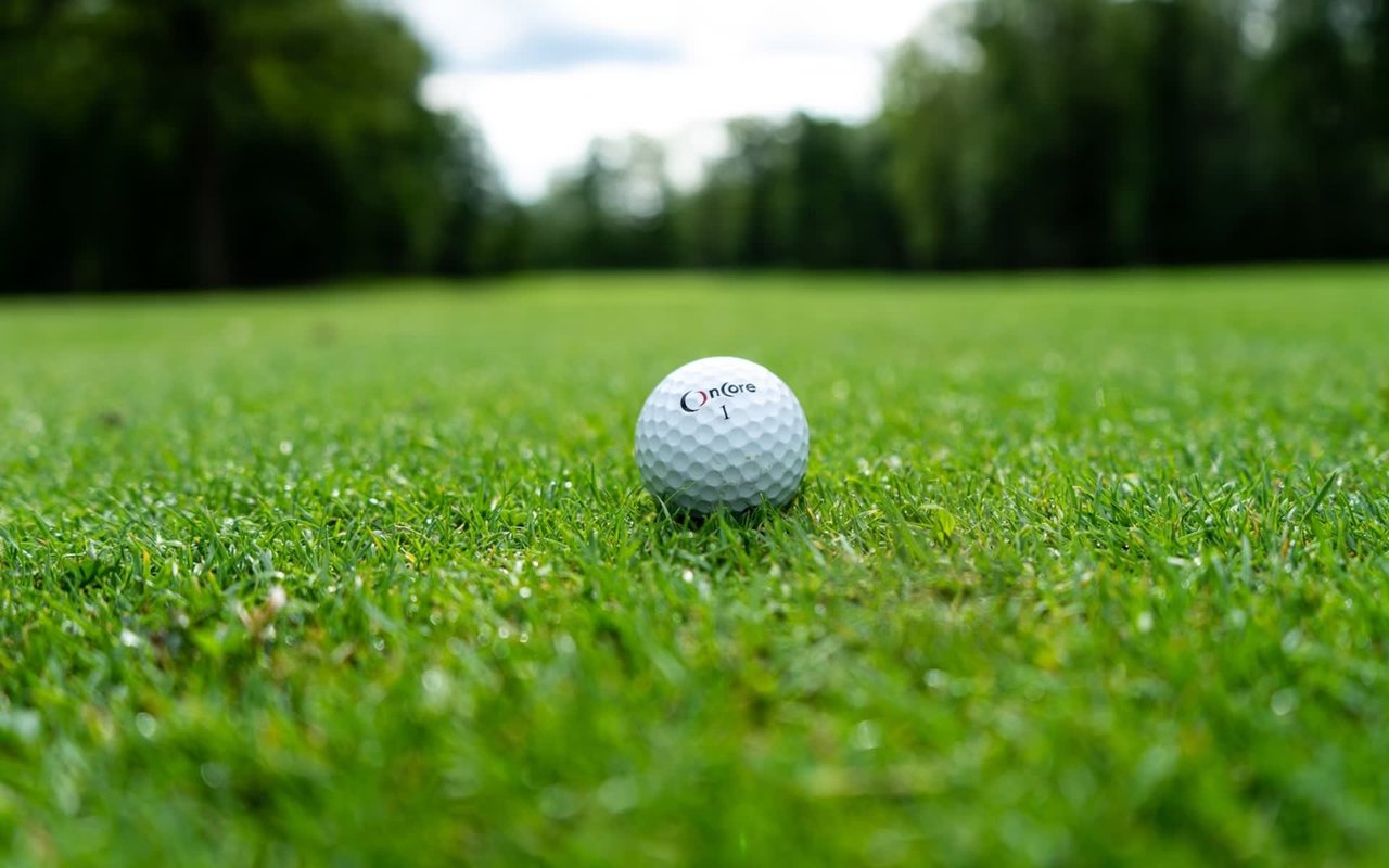 Close-up of an OnCore golf ball on a meticulously manicured green, highlighting the luxury golf community lifestyle with blurred fairway trees behind.