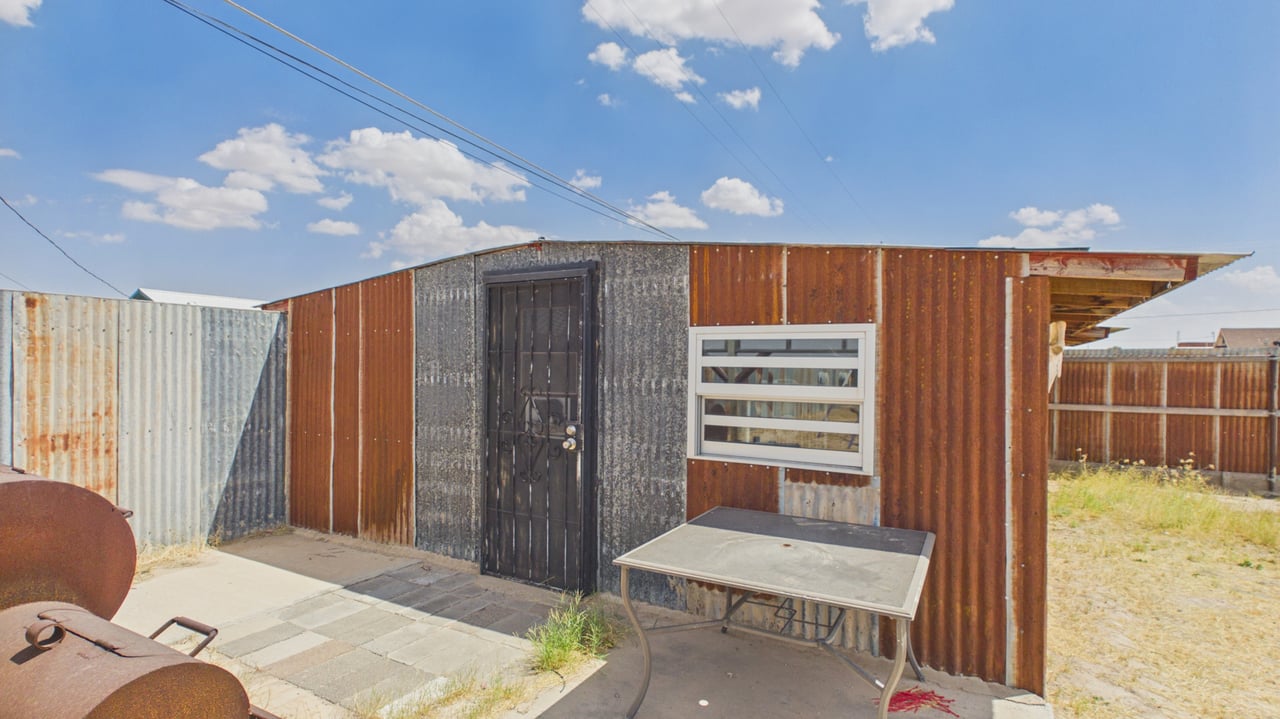 Corrugated-metal structure with a barred door, horizontal window, and projecting roof overhang.