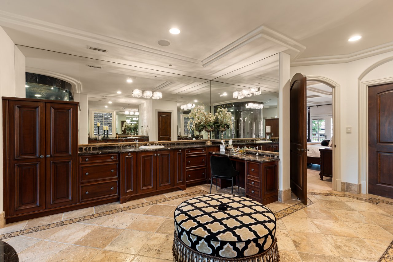 Luxury bathroom with dark wood vanities, expansive mirrors, and a round patterned stool.