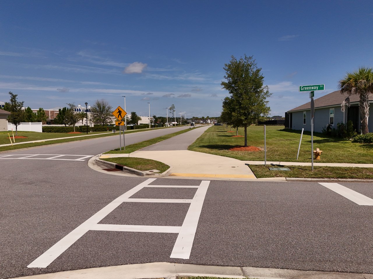 Neighborhood street with a crosswalk, sidewalks, lawns, and a Greenway Lane street sign.