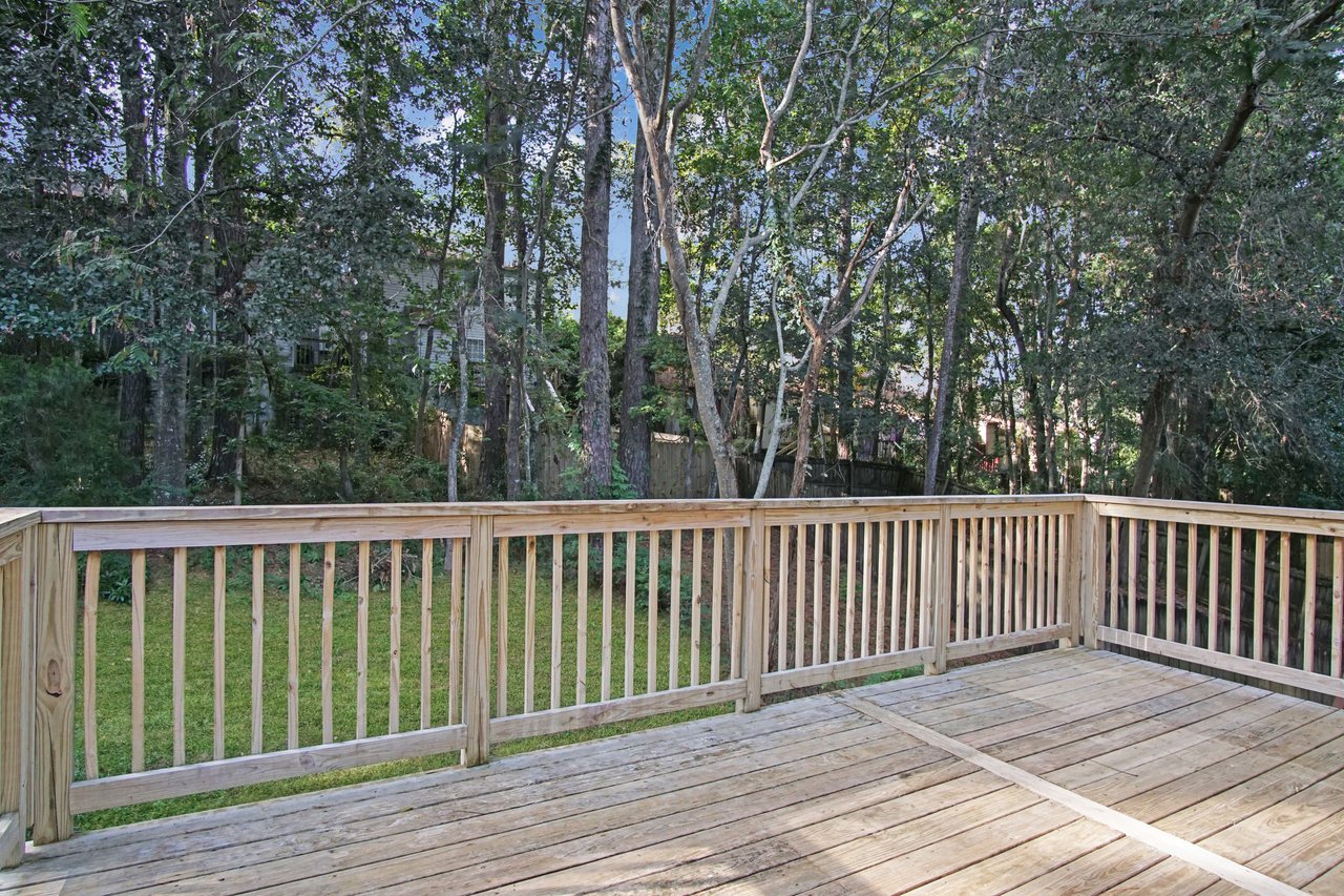 View from the back deck of 529 Collinsford Road, Tallahassee, Florida, showing a spacious wooden deck with railings overlooking a peaceful, tree-lined backyard. Tall pines and mature trees provide natural shade and privacy, creating a serene outdoor setting.