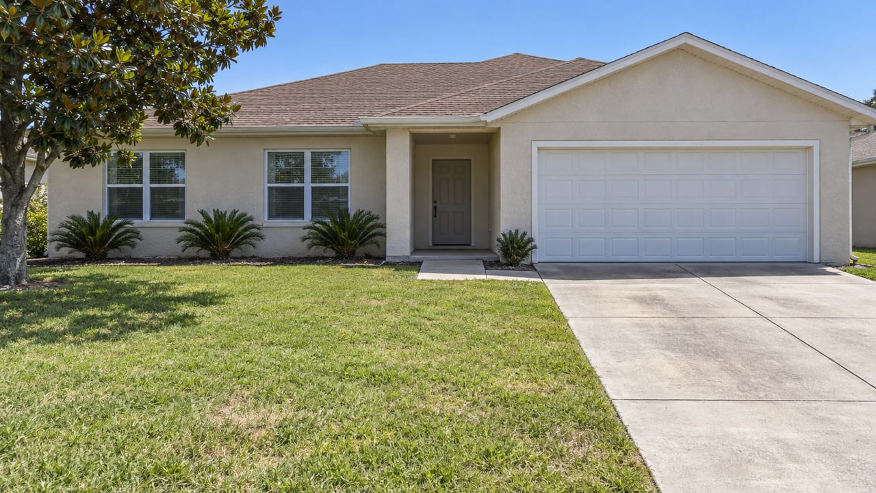 Sunlit single-story sand-colored stucco home with a brown shingle roof, white two-car garage, concrete driveway and green front lawn.