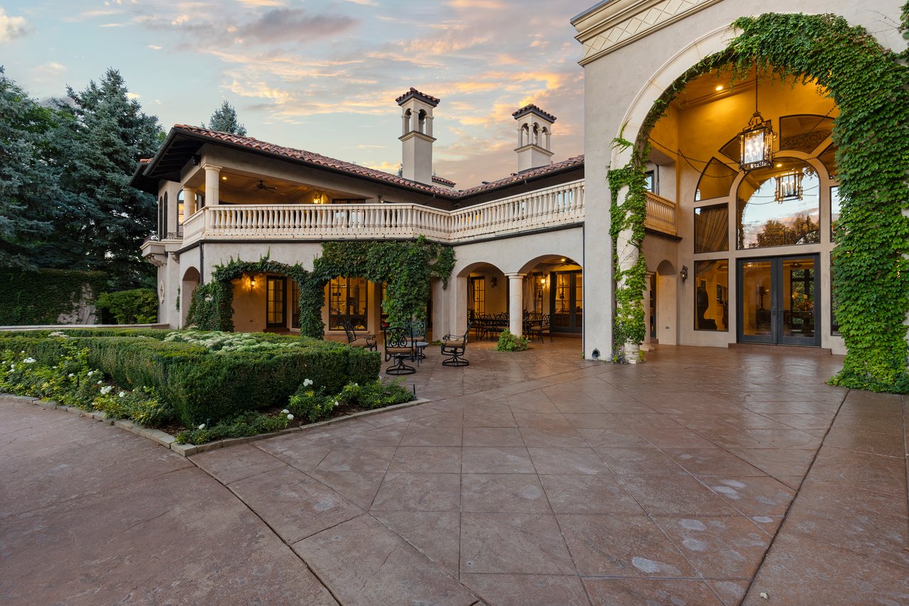 Estate courtyard with a broad stone patio, formal garden beds, and an ivy-framed arched entrance.